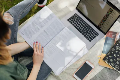 seseorang sedang membuka buku pelajaran dengan laptop di depannya.