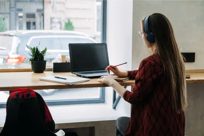 Seorang wanita sedang memakai headphones sambil menulis dan membuka laptop.