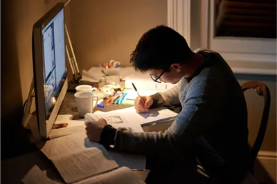 Seorang pria sedang belajar di depan laptop sambil menulis di buku tulis.