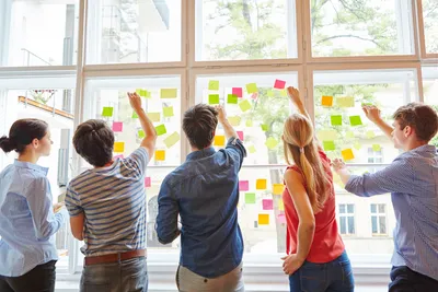 lima orang mahasiswa sedang berdiri menempelkan post it di kaca