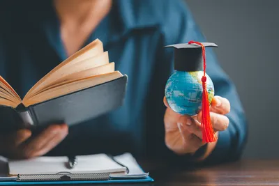 seseorang memegang buku dan globe yang pakai toga
